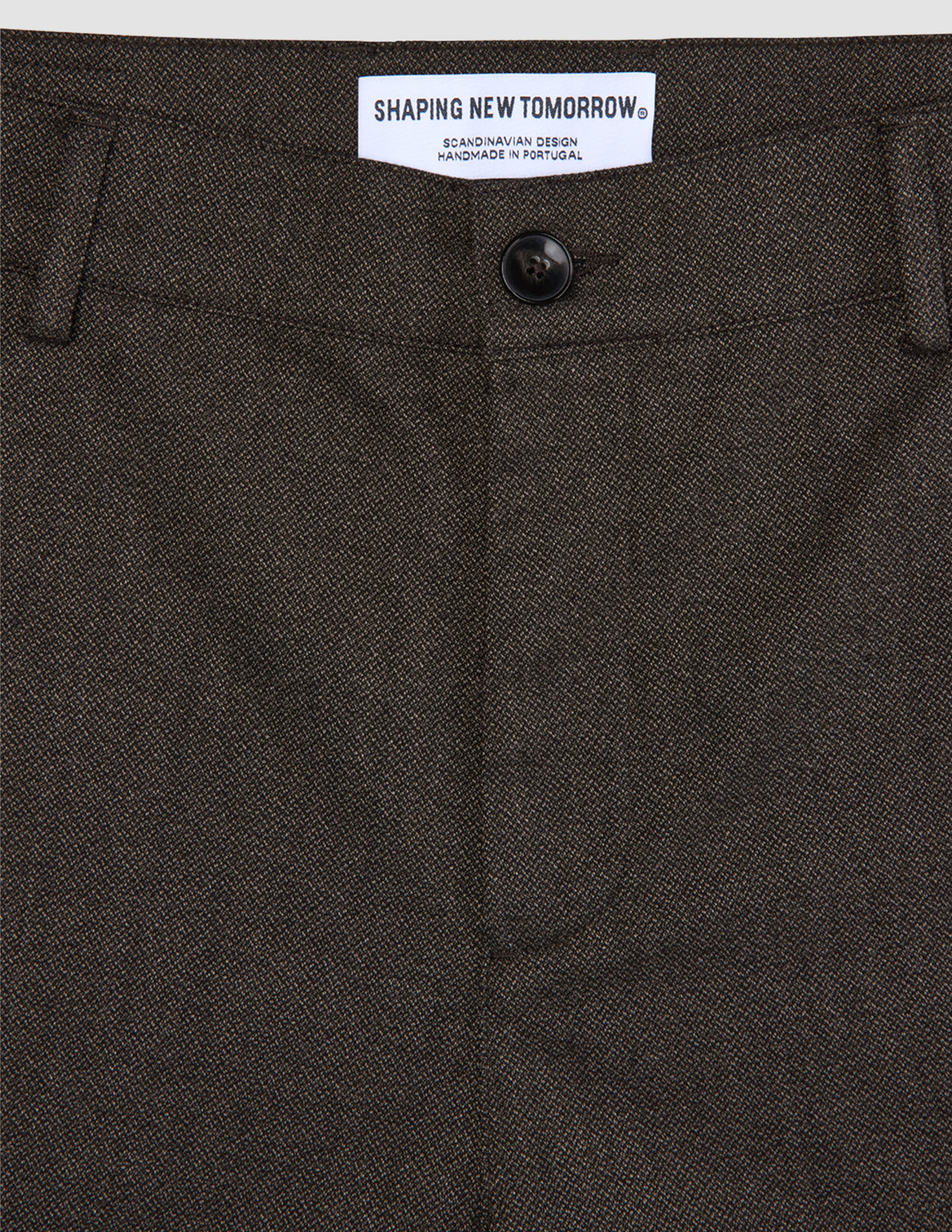 Nahaufnahme der Atelier Pants Relaxed in Dunkelbraun aus schwerem, gebrochenem Twill mit Knopfverschluss und Markenetikett am Bund.