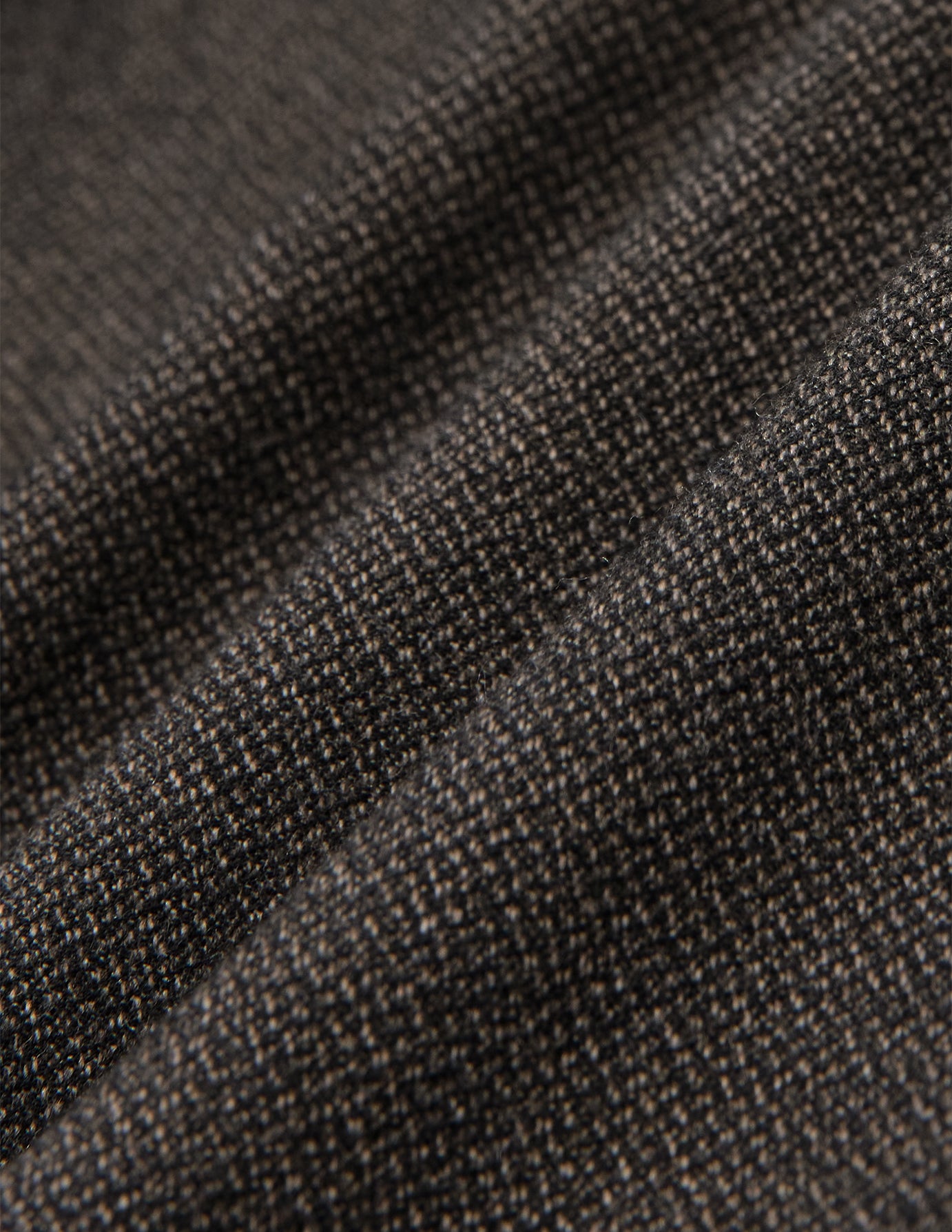 Nahaufnahme der Atelier Pants Relaxed Dark Brown aus gefaltetem, dunkelbraunem, schwerem Broken-Twill-Stoff mit strukturierter, gesprenkelter Webung und einem lässigen Schnitt.