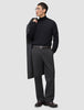 Ein Mann, der einen schwarzen Rollkragenpullover und eine Atelier Pants Relaxed in Dunkelgrau aus schwerem Broken-Twill trägt und einen Mantel über die Schulter gehängt hat.