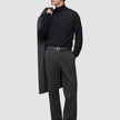 Ein Mann, der einen schwarzen Rollkragenpullover und eine Atelier Pants Relaxed in Dunkelgrau aus schwerem Broken-Twill trägt und einen Mantel über die Schulter gehängt hat.