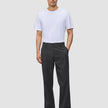 Ein Mann in einem weißen T-Shirt und einer Atelier Pants Relaxed in Dunkelgrau aus schwerem Broken-Twill, der vor einem einfarbigen Hintergrund steht.