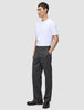 Eine Person in einem weißen T-Shirt und einer Atelier Pants Relaxed in Dunkelgrau aus schwerem Broken-Twill steht da, eine Hand in der Hosentasche.