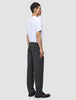 Ein Mann in einem weißen T-Shirt und einer Atelier Pants Relaxed in Dunkelgrau aus schwerem, gebrochenem Twill, im Profil stehend.