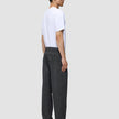 Ein Mann in einem weißen T-Shirt und einer Atelier Pants Relaxed in Dunkelgrau aus schwerem, gebrochenem Twill, im Profil stehend.