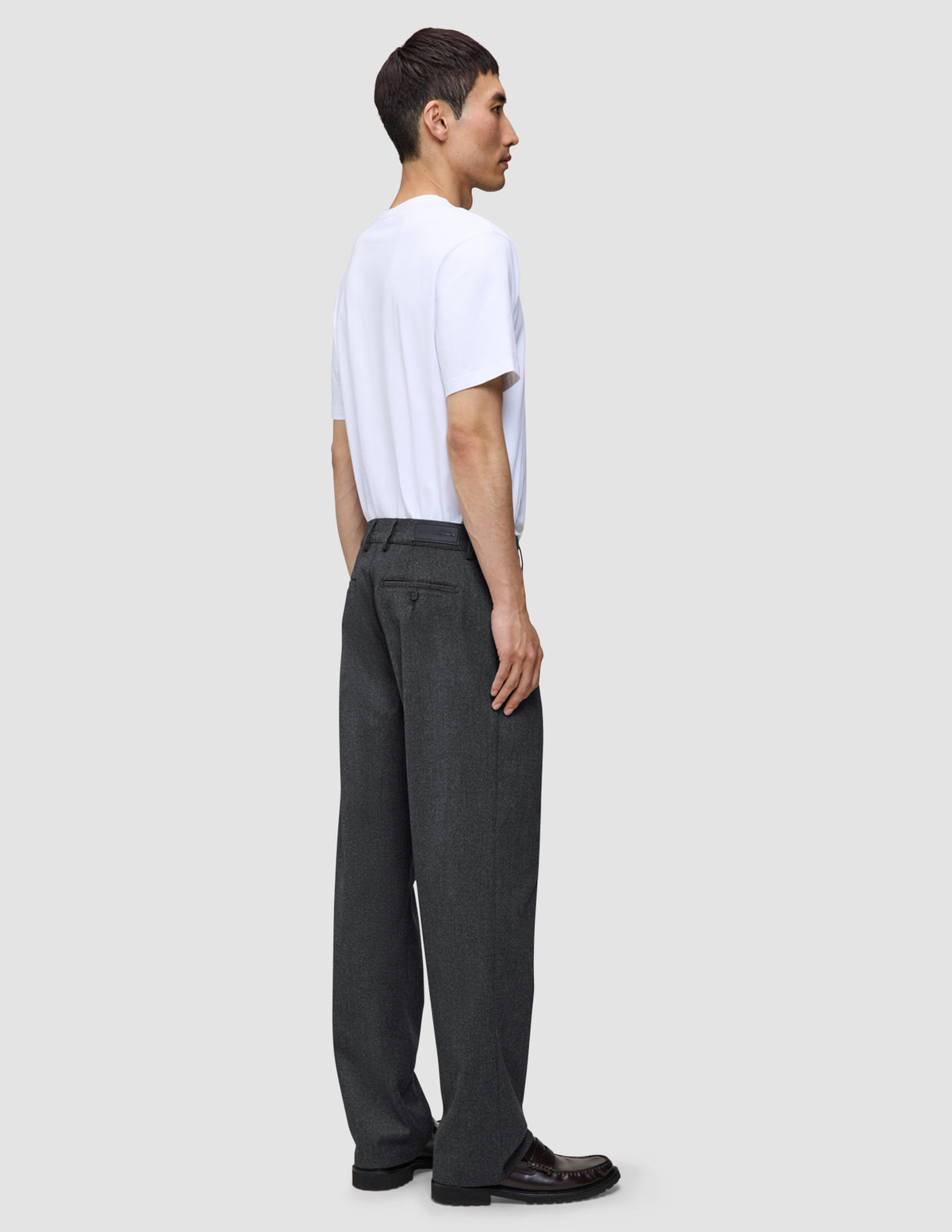 Ein Mann in einem weißen T-Shirt und einer Atelier Pants Relaxed in Dunkelgrau aus schwerem, gebrochenem Twill, im Profil stehend.