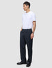 Ein Mann, der ein weißes T-Shirt und eine Atelier Pants Relaxed Dark Navy aus schwerem, gebrochenem Twill trägt, steht vor einem einfarbigen Hintergrund.