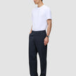 Ein Mann, der ein weißes T-Shirt und eine Atelier Pants Relaxed Dark Navy aus schwerem, gebrochenem Twill trägt, steht vor einem einfarbigen Hintergrund.