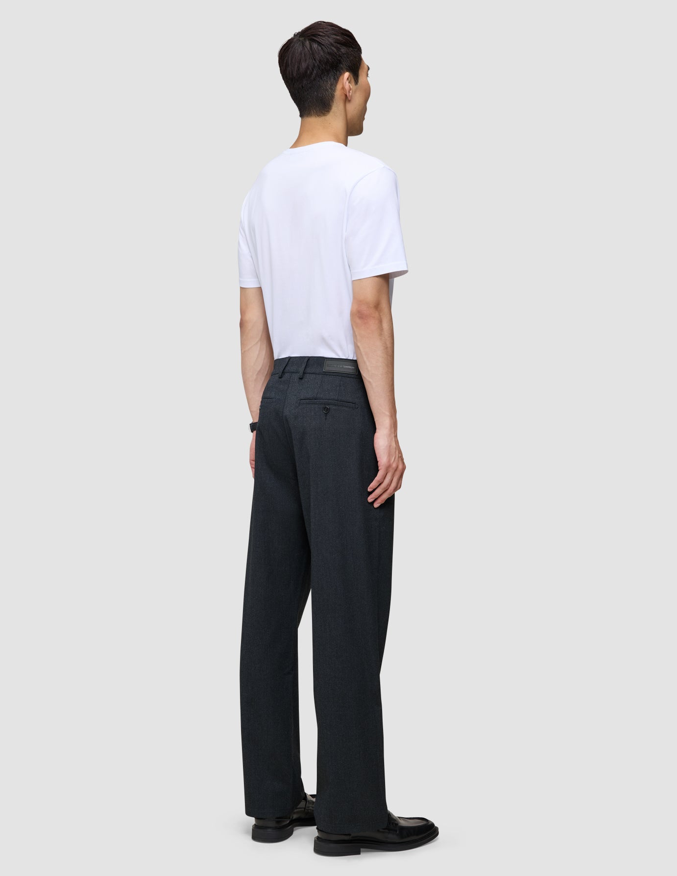 Ein Mann, von hinten gesehen, der ein weißes T-Shirt und eine Atelier Pants Relaxed Dark Navy aus schwerem, gebrochenem Twill trägt.