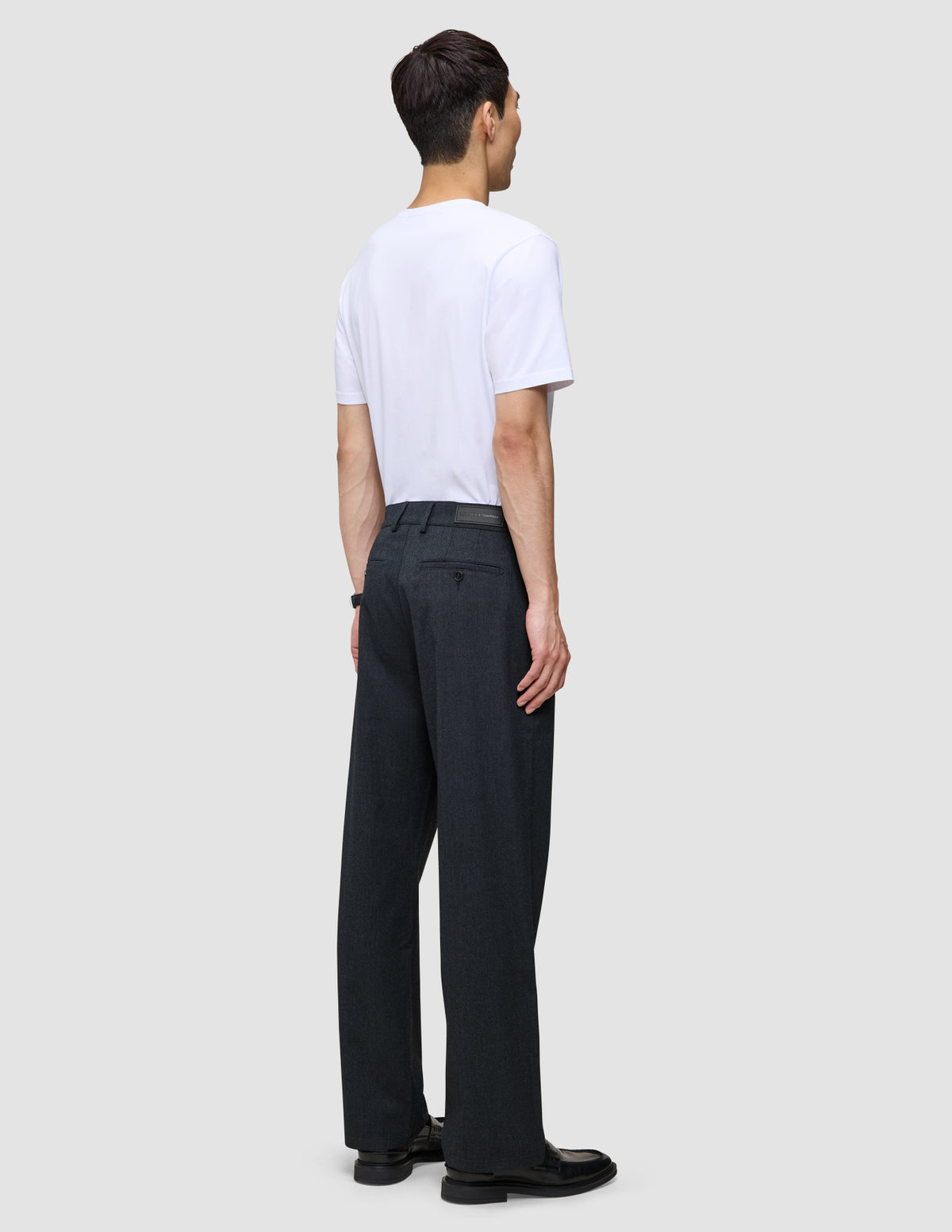 Ein Mann, von hinten gesehen, der ein weißes T-Shirt und eine Atelier Pants Relaxed Dark Navy aus schwerem, gebrochenem Twill trägt.