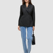 Eine Frau, die einen schwarzen, zweireihigen Women’s Avira Blazer Black-Blazer, eine blaue Jeans und dunkle Pumps trägt und eine kleine schwarze Handtasche in der Hand hält.
