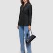 Eine Frau trägt einen schwarzen, zweireihigen Avira Blazer Black-Damenblazer zu einer blauen Jeans und hat eine schwarze Handtasche dabei.