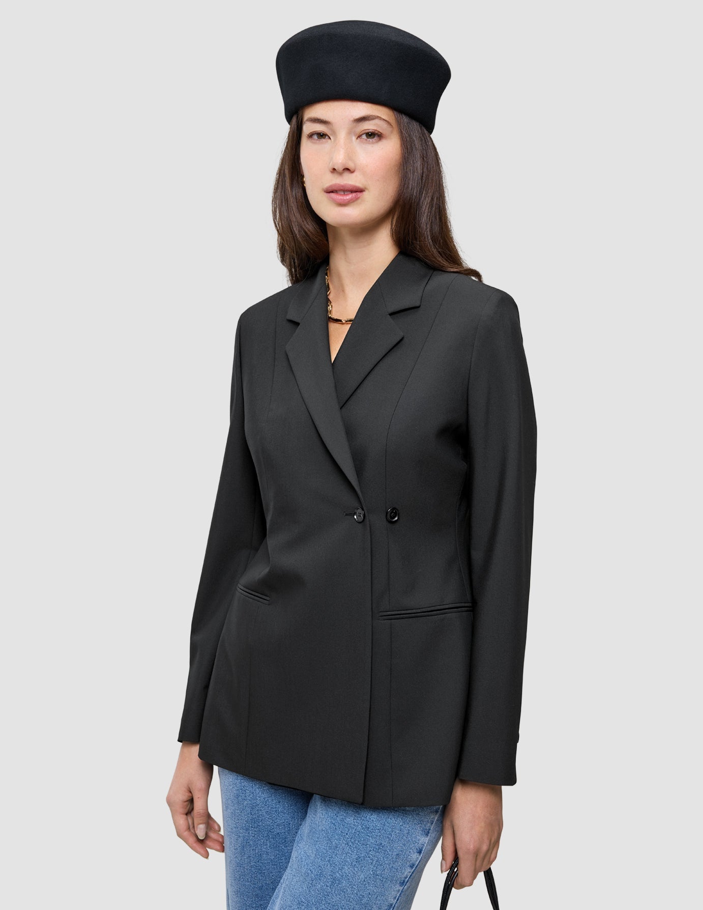 Eine Person, die einen schwarzen, zweireihigen Avira Blazer Black-Damenblazer und eine schwarze Baskenmütze im skandinavischen Stil trägt.