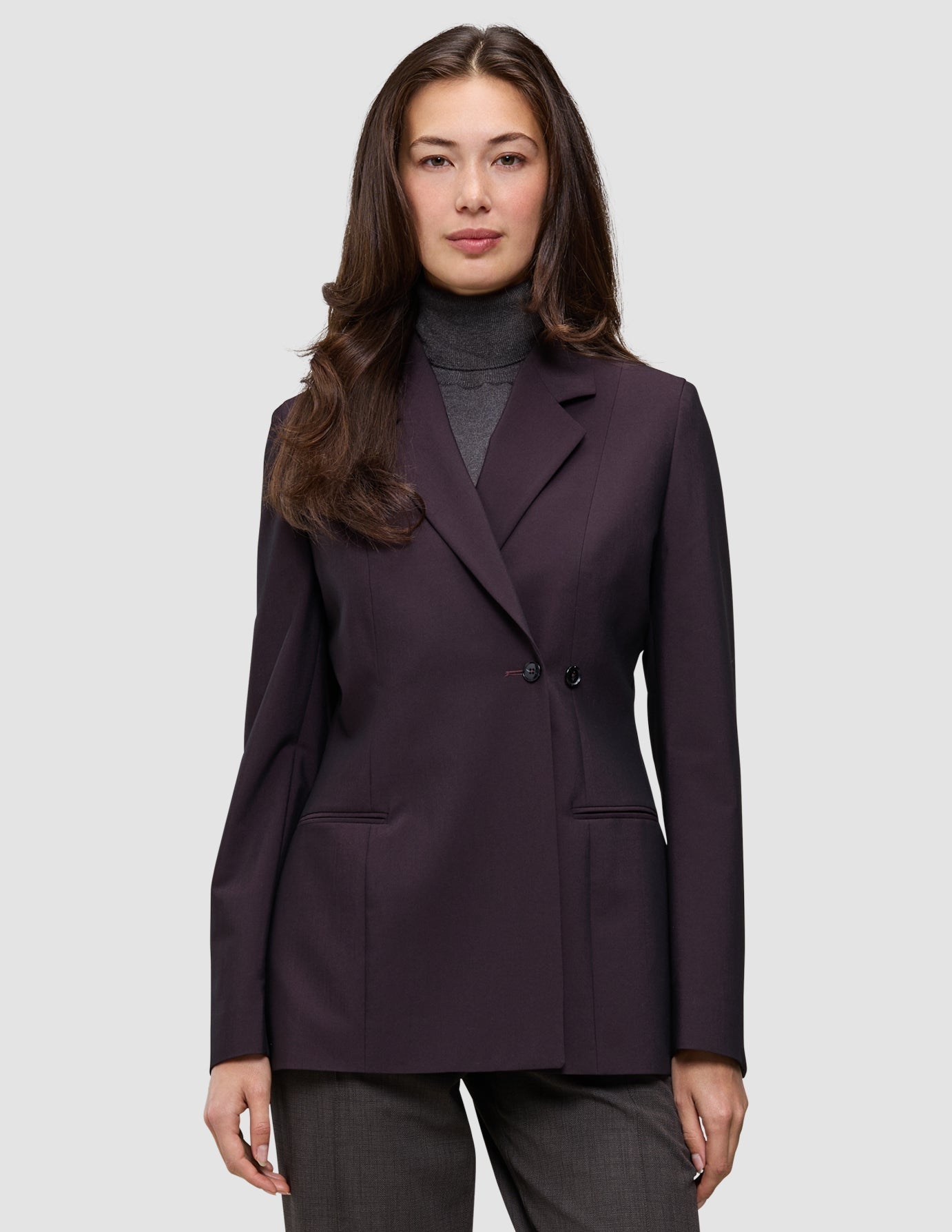 Ein Model trägt den Damenblazer Avira in der Farbe Burgundy Berry – einen dunkelburgunderroten Zweireiher im minimalistischen skandinavischen Design – über einem grauen Rollkragenpullover.