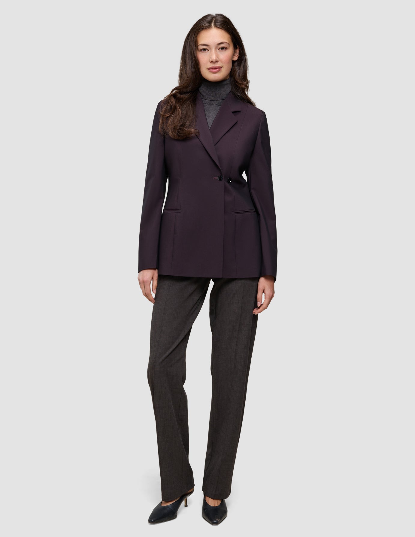Eine Person, die einen Avira-Blazer für Damen in der Farbe Burgundy Berry im skandinavischen Zweireiher-Design über einem grauen Rollkragenpullover und einer dunklen Hose trägt.