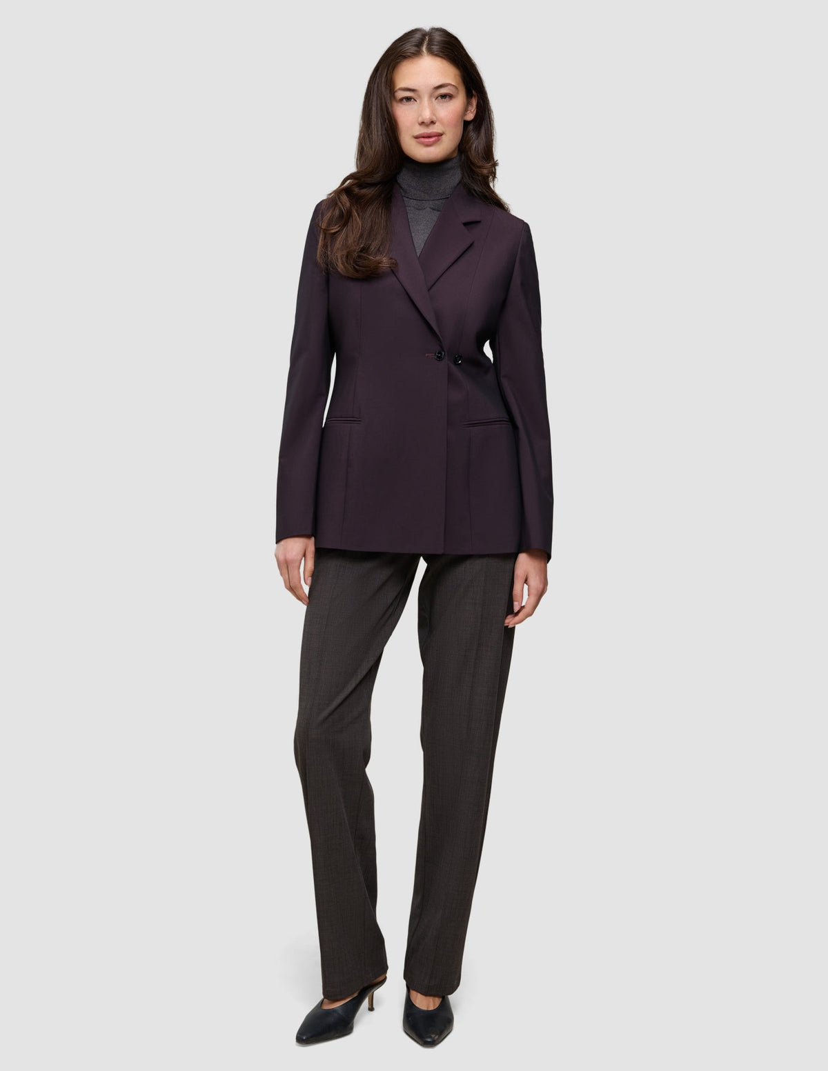Eine Person, die einen Avira-Blazer für Damen in der Farbe Burgundy Berry im skandinavischen Zweireiher-Design über einem grauen Rollkragenpullover und einer dunklen Hose trägt.