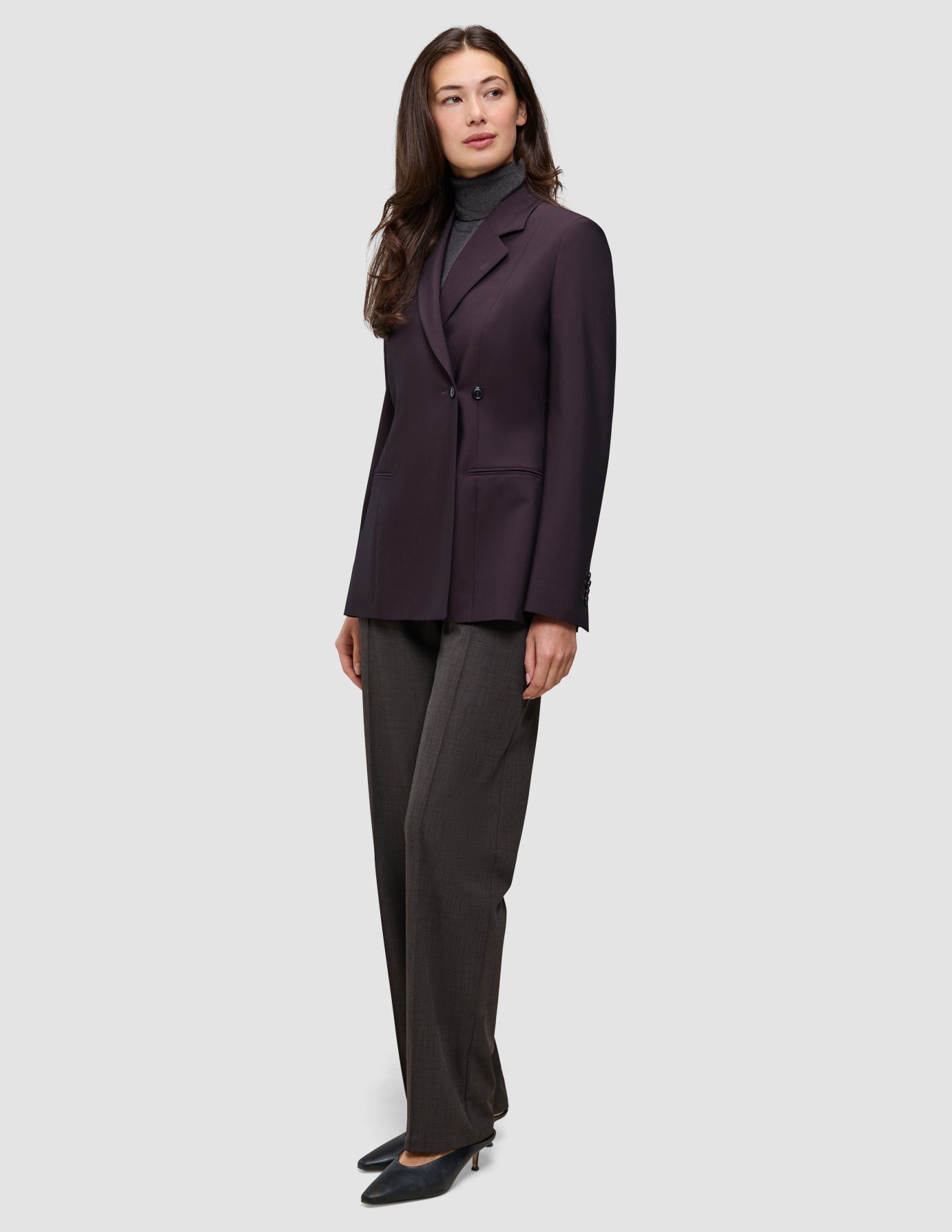 Eine Frau trägt einen burgunderroten Avira-Damenblazer in der Farbe Burgundy Berry im skandinavischen Zweireiher-Design über einem grauen Rollkragenpullover und einer dunklen Hose.