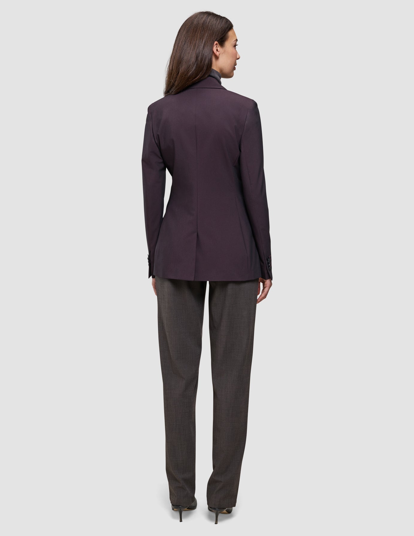 Rückansicht einer Frau, die einen dunkelburgunderroten Avira-Damenblazer in der Farbe Burgundy Berry und eine anthrazitfarbene Hose im eleganten skandinavischen Design trägt.