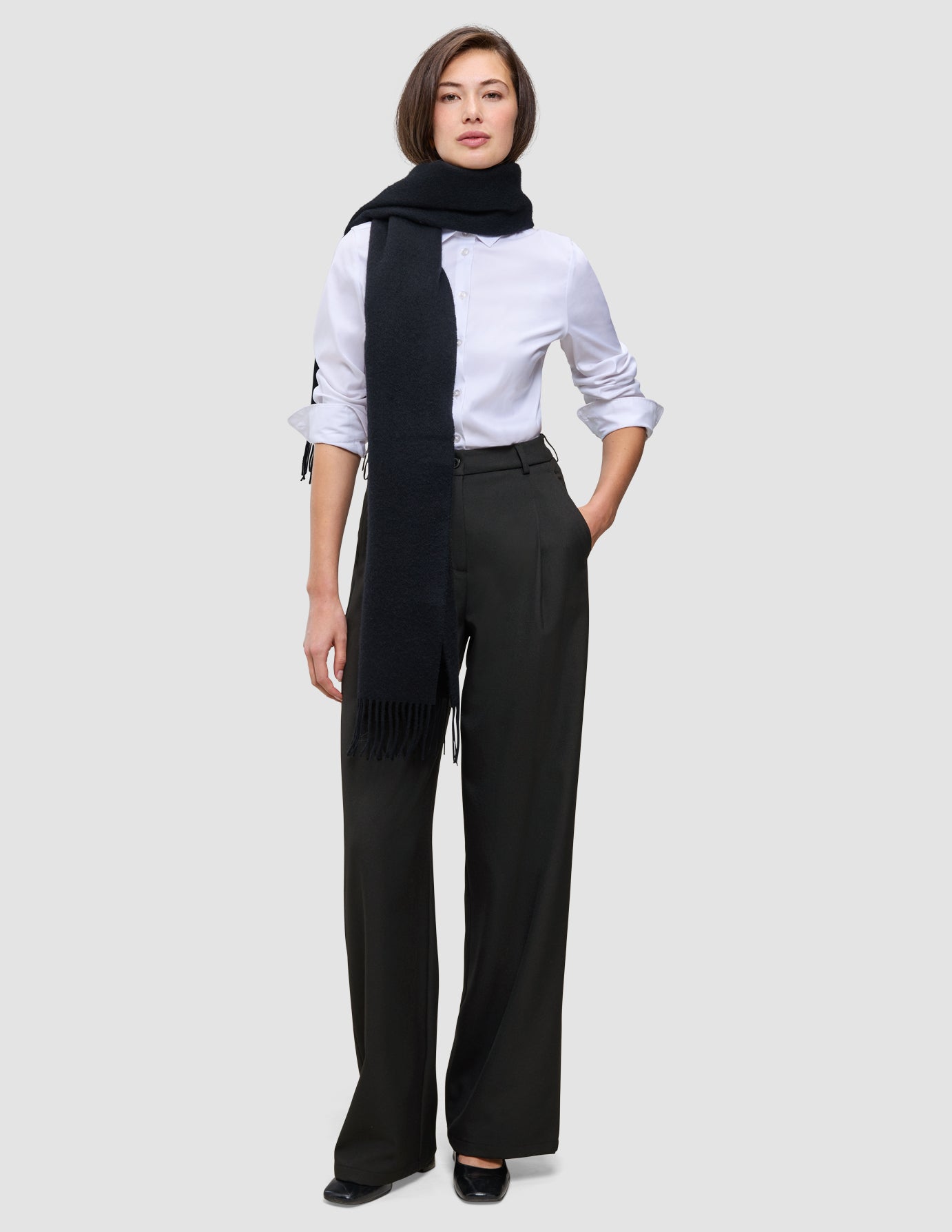 Eine Frau, die ein weißes Hemd, einen schwarzen Schal und die Damenhose Avira Pants Wide Black trägt.