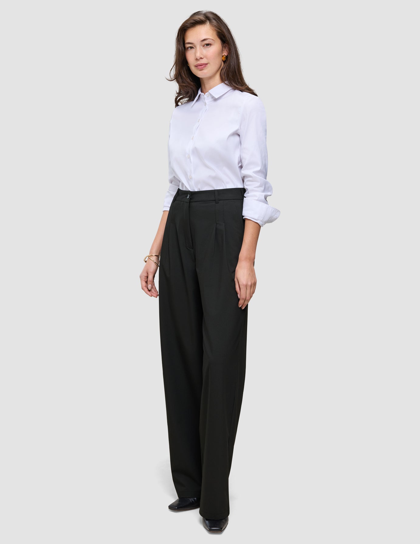Eine Frau, die ein weißes Hemd trägt, das in eine schwarze Damenhose Avira Pants Wide mit hoher Taille gesteckt ist.