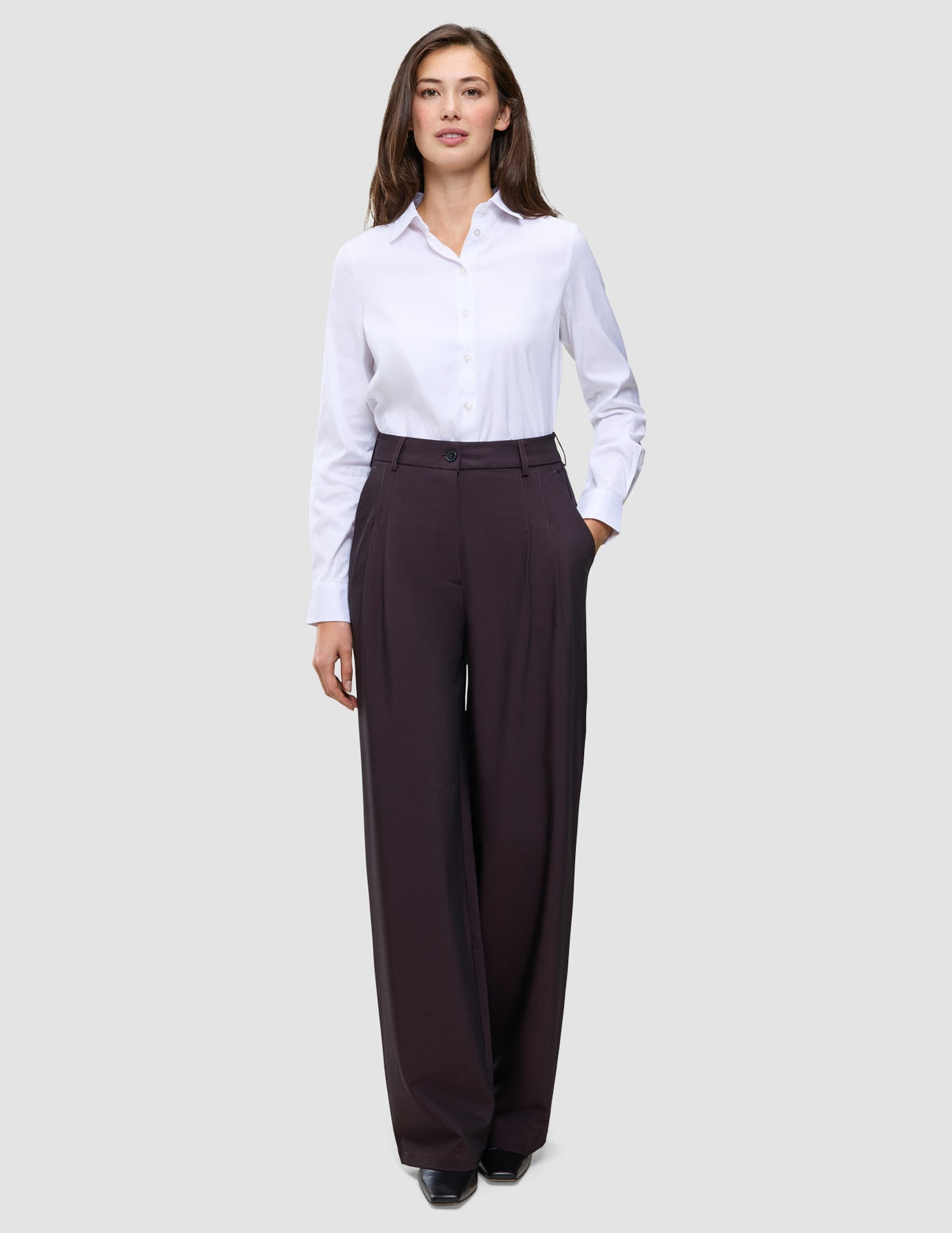 Eine Person, die ein weißes, langärmeliges Hemd mit Knöpfen trägt, das in die Damenhose Avira Pants Wide in der Farbe Burgundy Berry gesteckt ist.