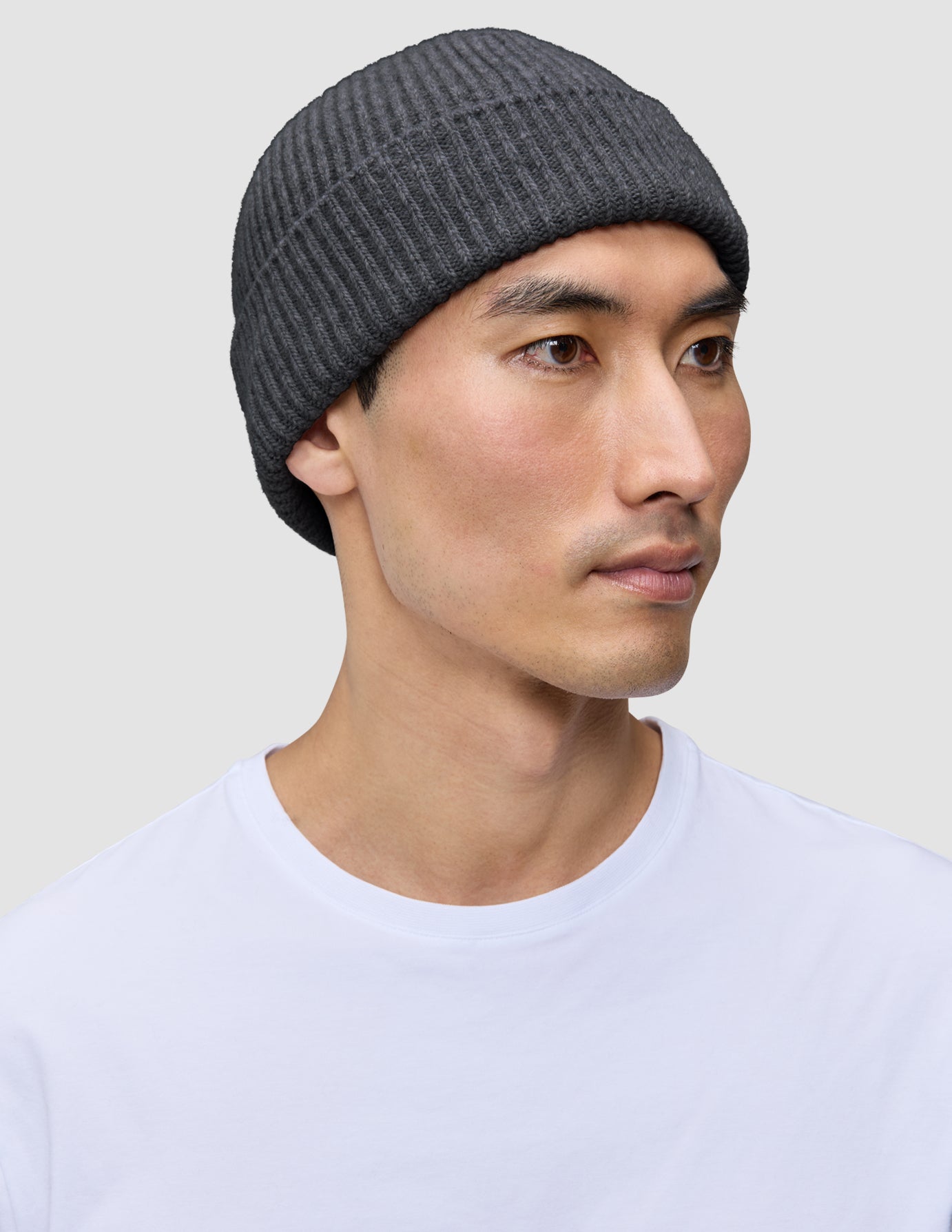 Eine Person, die eine dunkelgraue Mütze (Beanie Dark Grey) mit minimalistischem skandinavischem Design und gerippter Strickstruktur trägt.