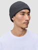 Eine Person, die eine dunkelgraue Mütze (Beanie Dark Grey) mit minimalistischem skandinavischem Design und gerippter Strickstruktur trägt.