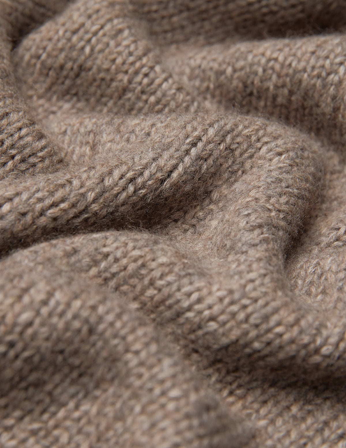 Nahaufnahme einer Damen-Strickjacke aus weicher, grobstrickiger Wolle in Taupe-Melange, die sich durch eine dicke, taupefarbene Grobstrick-Struktur aus Merinowolle auszeichnet.