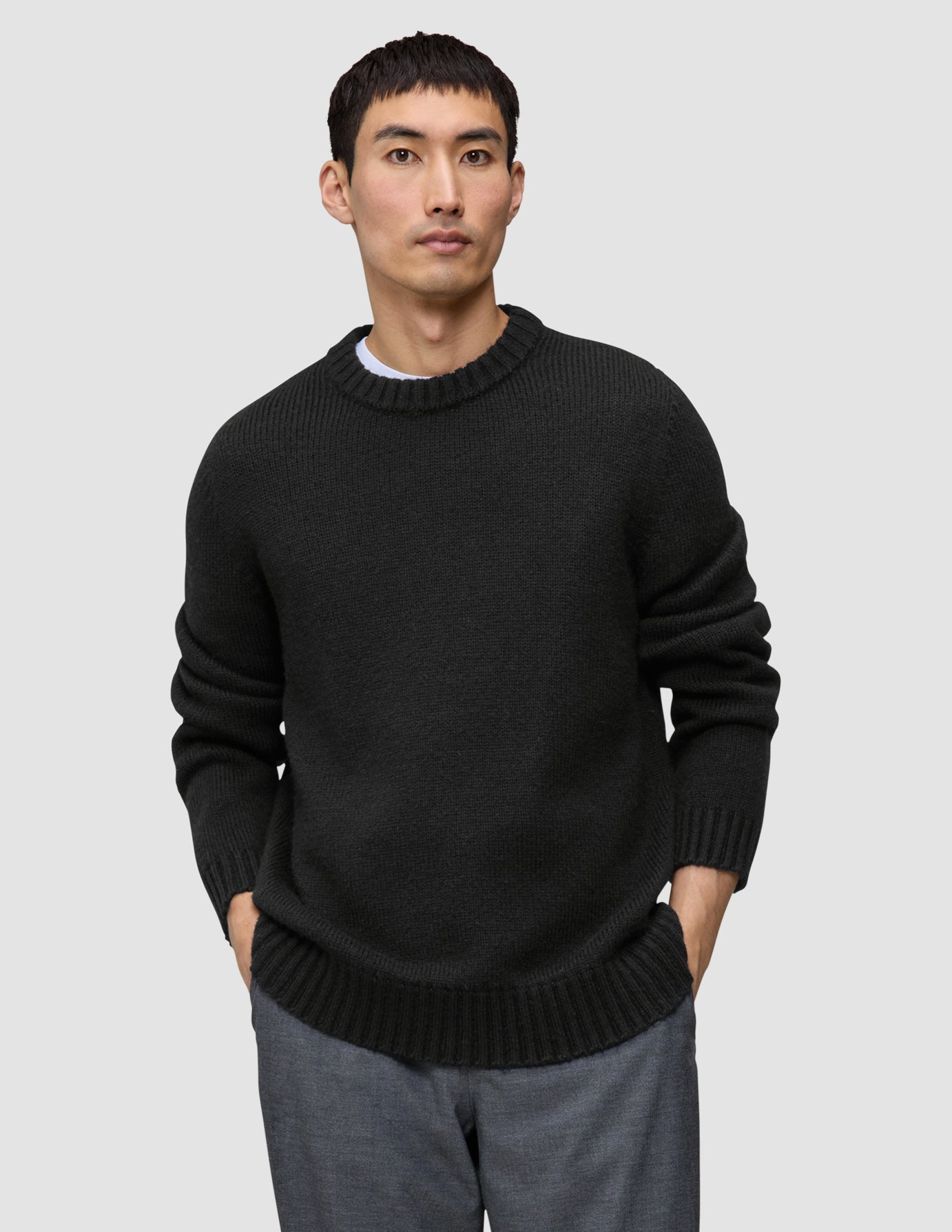 Ein Mann, der einen schwarzen, grob gestrickten Pullover aus weicher Wolle mit Rundhalsausschnitt, dickem Kragen und gerippten Bündchen trägt.