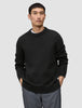 Ein Mann, der einen schwarzen, grob gestrickten Pullover aus weicher Wolle mit Rundhalsausschnitt, dickem Kragen und gerippten Bündchen trägt.