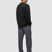 Eine Person im Profil, die einen schwarzen, grob gestrickten, weichen Wollpullover mit Rundhalsausschnitt und eine graue Hose trägt.