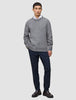 Ein Mann, der einen dicken, weichen Wollpullover mit Rundhalsausschnitt in Gletschergrau über einem weißen Hemd mit Kragen, einer dunklen Hose und braunen Slippern trägt.