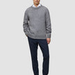 Ein Mann, der einen dicken, weichen Wollpullover mit Rundhalsausschnitt in der Farbe Glacier Grey über einem weißen Hemd mit Kragen, einer dunklen Hose und Loafern trägt.