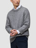 Ein Mann trägt einen dicken, weichen Wollpullover mit Rundhalsausschnitt in der Farbe Glacier Grey über einem weißen Hemd mit Kragen.