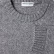 Nahaufnahme eines grauen, grob gestrickten, weichen Wollpullovers mit Rundhalsausschnitt in der Farbe Glacier Grey, der sich durch einen gerippten Kragen und gerippte Ärmelbündchen auszeichnet.