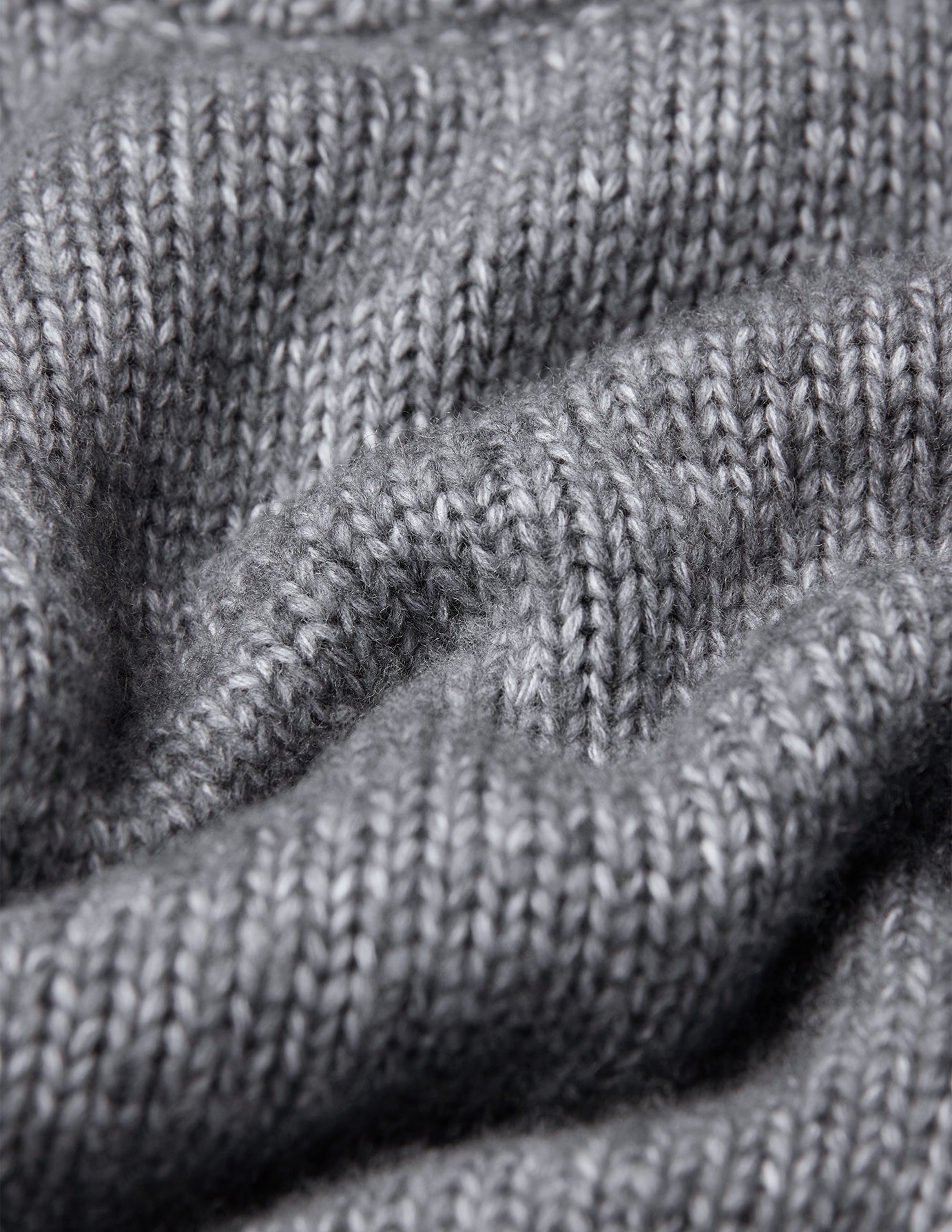 Nahaufnahme eines grauen, grob gestrickten, weichen Wollpullovers mit Rundhalsausschnitt in der Farbe Glacier Grey und strukturierter Rippenstrickoptik.