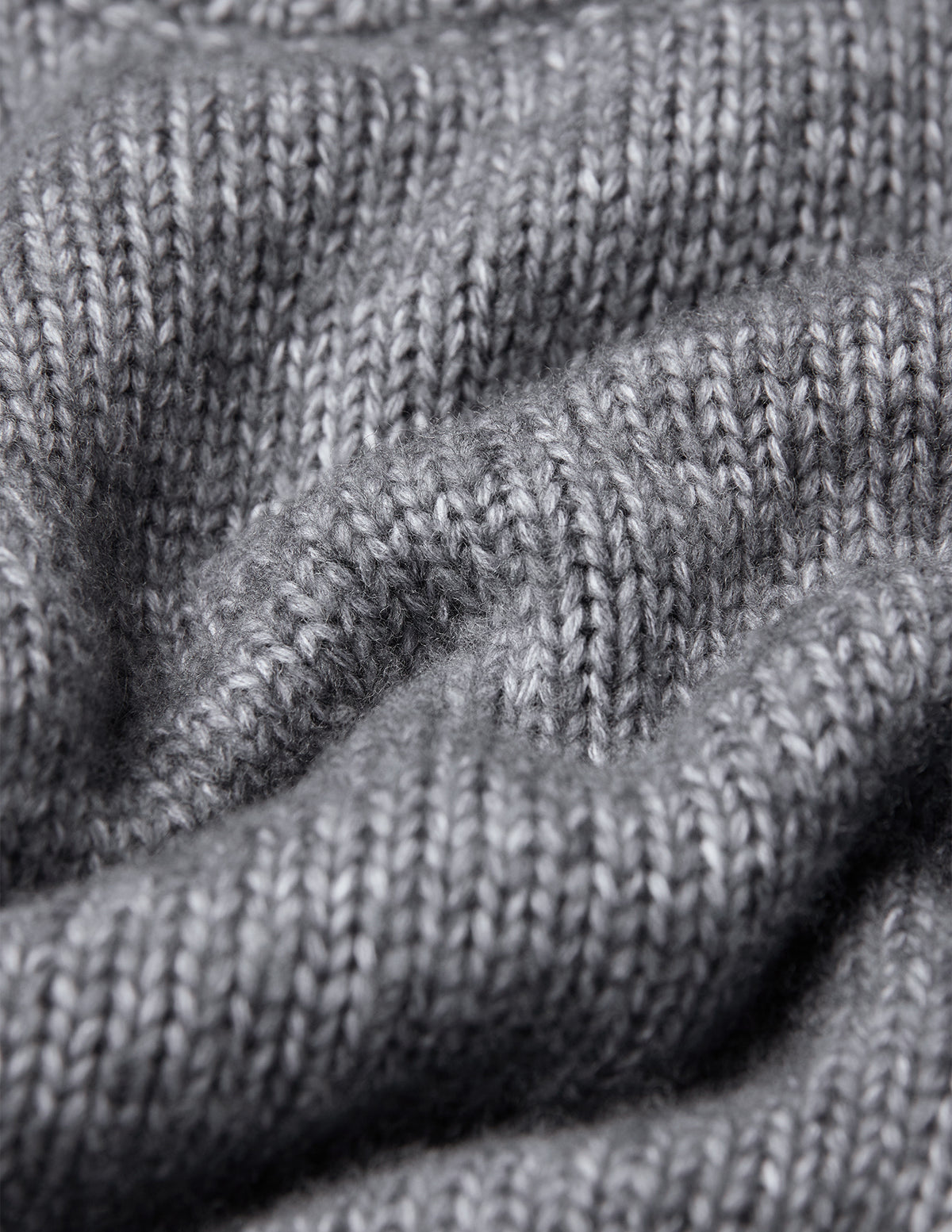 Nahaufnahme eines grauen, grob gestrickten, weichen Wollpullovers mit Rundhalsausschnitt in der Farbe Glacier Grey und strukturierter Rippenstrickoptik.