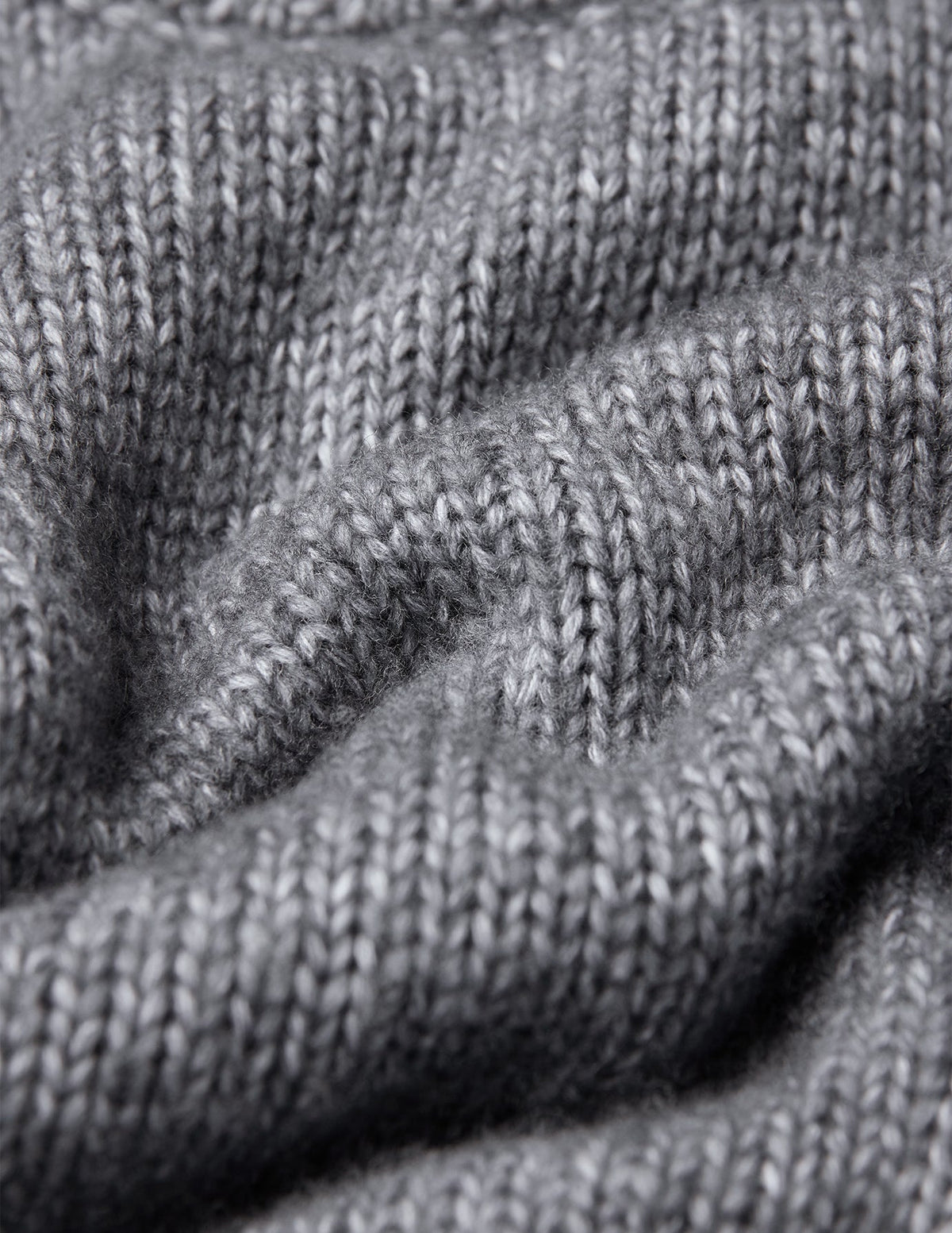 Nahaufnahme eines grauen, grob gestrickten, weichen Wollpullovers mit Rundhalsausschnitt in der Farbe Glacier Grey, der sich durch eine deutlich sichtbare Rippenstruktur auszeichnet.
