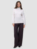 Eine Frau, die einen Damen-Rollkragenpullover aus dicker, weicher Wolle in der Farbe Sugar Melange in Off-White und eine dunkle Hose mit weitem Bein trägt.