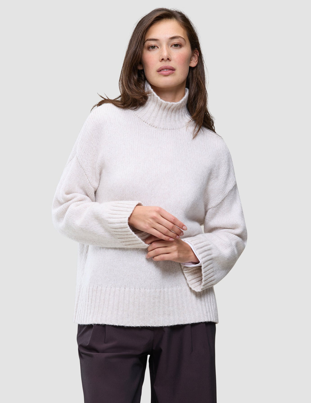Eine Frau, die einen cremefarbenen Damen-Rollkragenpullover aus dickem, weichem Wollstrick in der Farbe Sugar Melange mit weiten Ärmeln trägt.