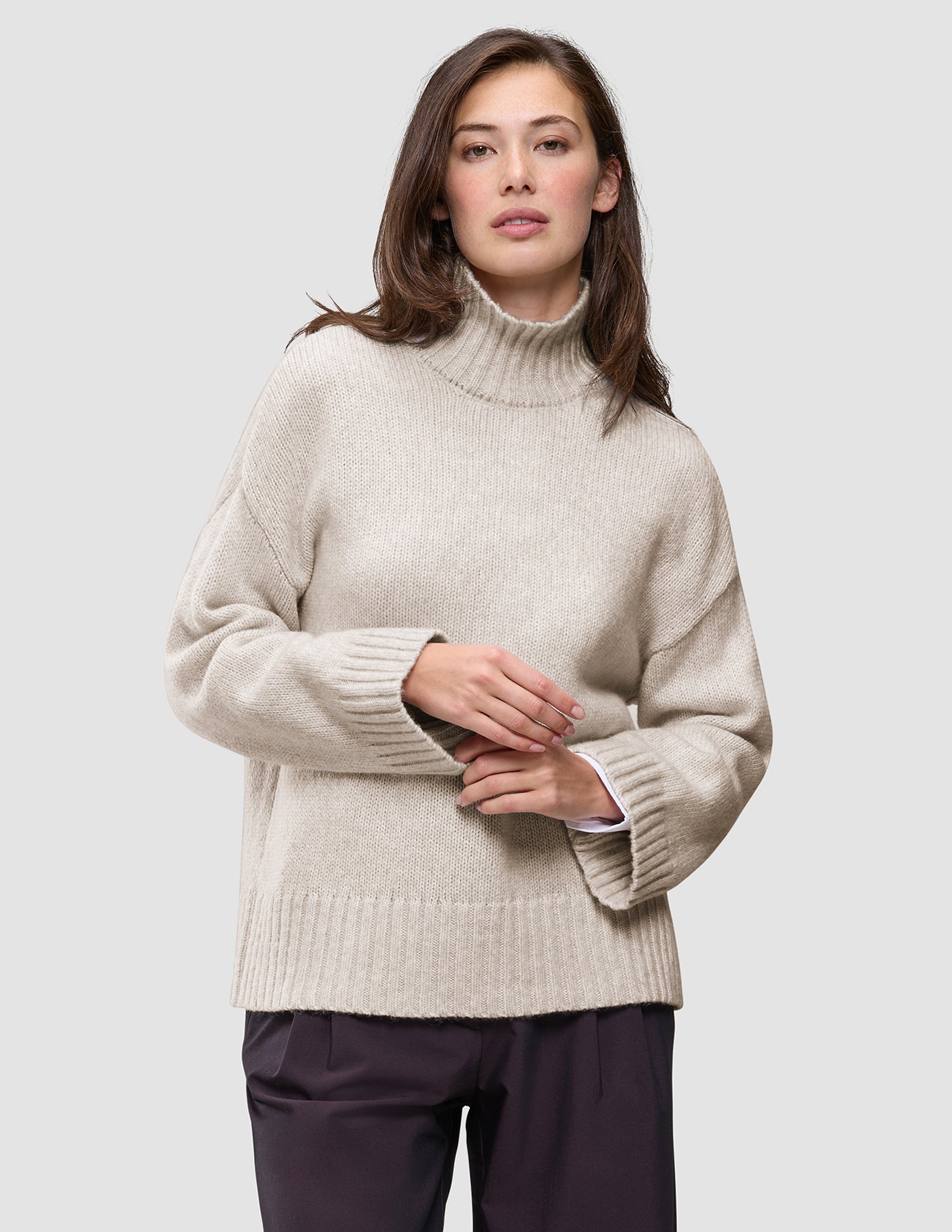 Eine Frau trägt einen übergroßen, beigen Damen-Rollkragenpullover aus weicher, grobstrickiger Wolle in der Farbe Sugar Melange mit überschnittenen Schultern.