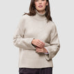 Eine Frau trägt einen übergroßen, beigen Damen-Rollkragenpullover aus weicher, grobstrickiger Wolle in der Farbe Sugar Melange mit überschnittenen Schultern.