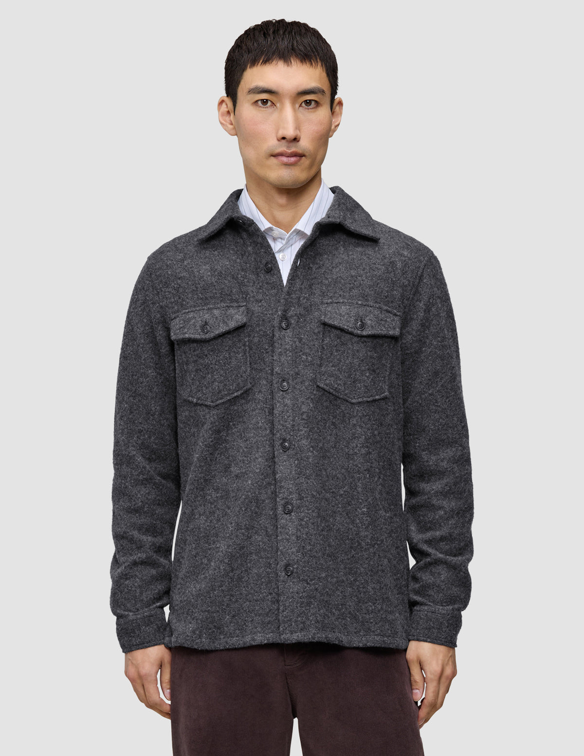 Ein Mann trägt ein doppellagiges Woll-Overshirt in der Farbe Regular Dark Grey über einem weißen Hemd mit Kragen, das ein minimalistisches skandinavisches Design widerspiegelt.