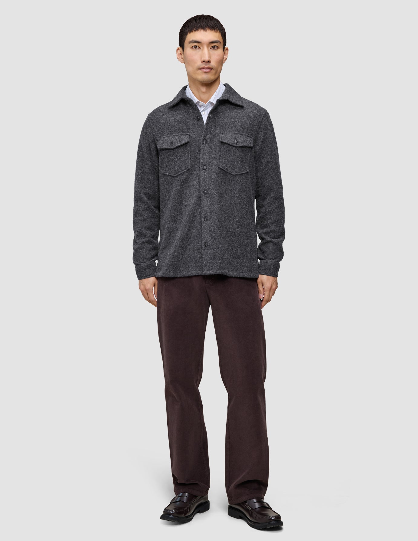 Ein Mann trägt ein doppellagiges Woll-Overshirt in Regular-Passform in Dunkelgrau über einem weißen Hemd, dazu eine dunkle Hose und schwarze Loafer im skandinavischen Design.