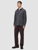 Ein Mann, der ein doppellagiges Woll-Overshirt in Regular-Passform und Dunkelgrau über einem weißen Hemd mit Kragen trägt, dazu eine dunkle Hose und braune Slipper in einem schlichten, skandinavischen Design.