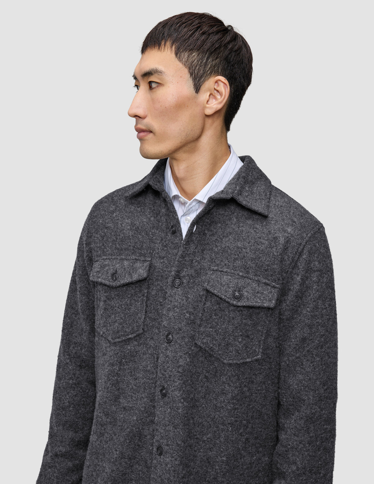 Ein Mann, der ein doppellagiges Woll-Overshirt in der Farbe Regular Dark Grey über einem Hemd mit Kragen trägt, das sich durch ein klares, skandinavisches Design auszeichnet.