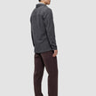 Eine Person, von hinten gesehen, die ein doppellagiges Woll-Overshirt in der Ausführung Regular in Dunkelgrau, eine dunkelbraune Hose und schwarze Slipper trägt.