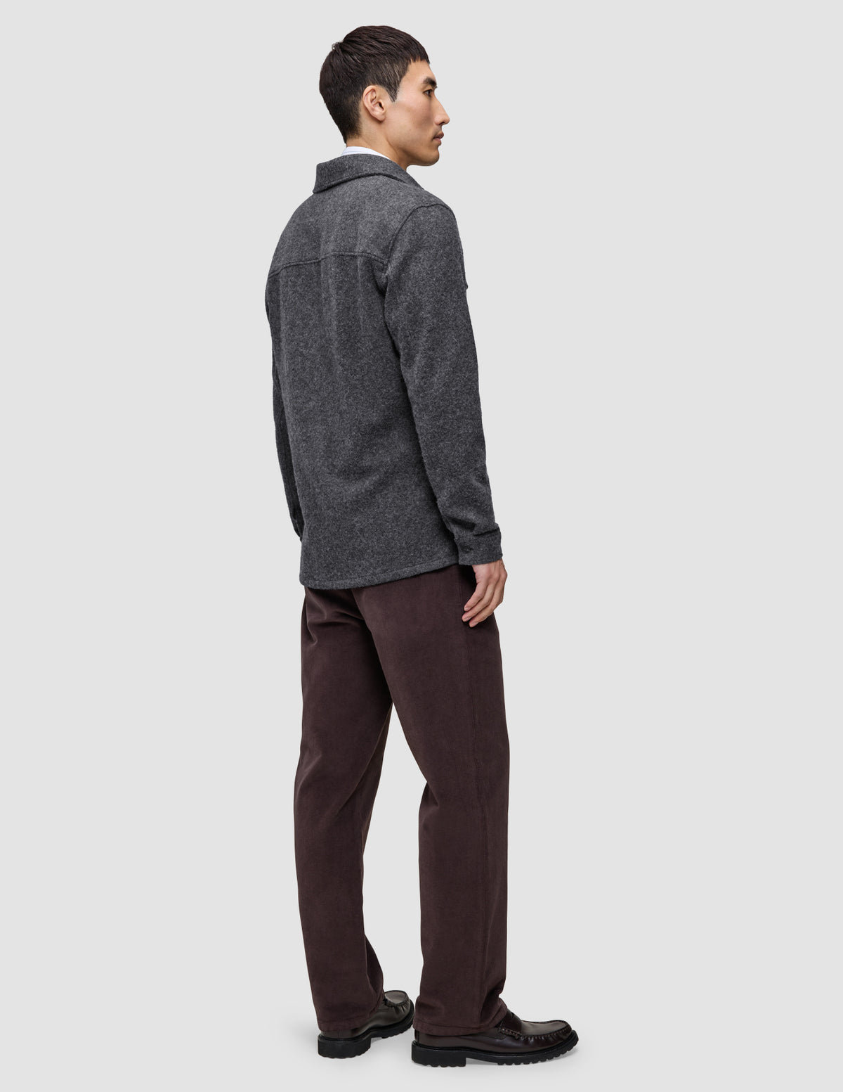 Eine Person, von hinten gesehen, die ein doppellagiges Woll-Overshirt in der Ausführung Regular in Dunkelgrau, eine dunkelbraune Hose und schwarze Slipper trägt.