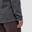 Nahaufnahme einer Person, die ein dunkelgraues, doppellagiges Woll-Overshirt in regulärer Passform mit geknöpften Manschetten trägt, kombiniert mit einer braunen Hose.