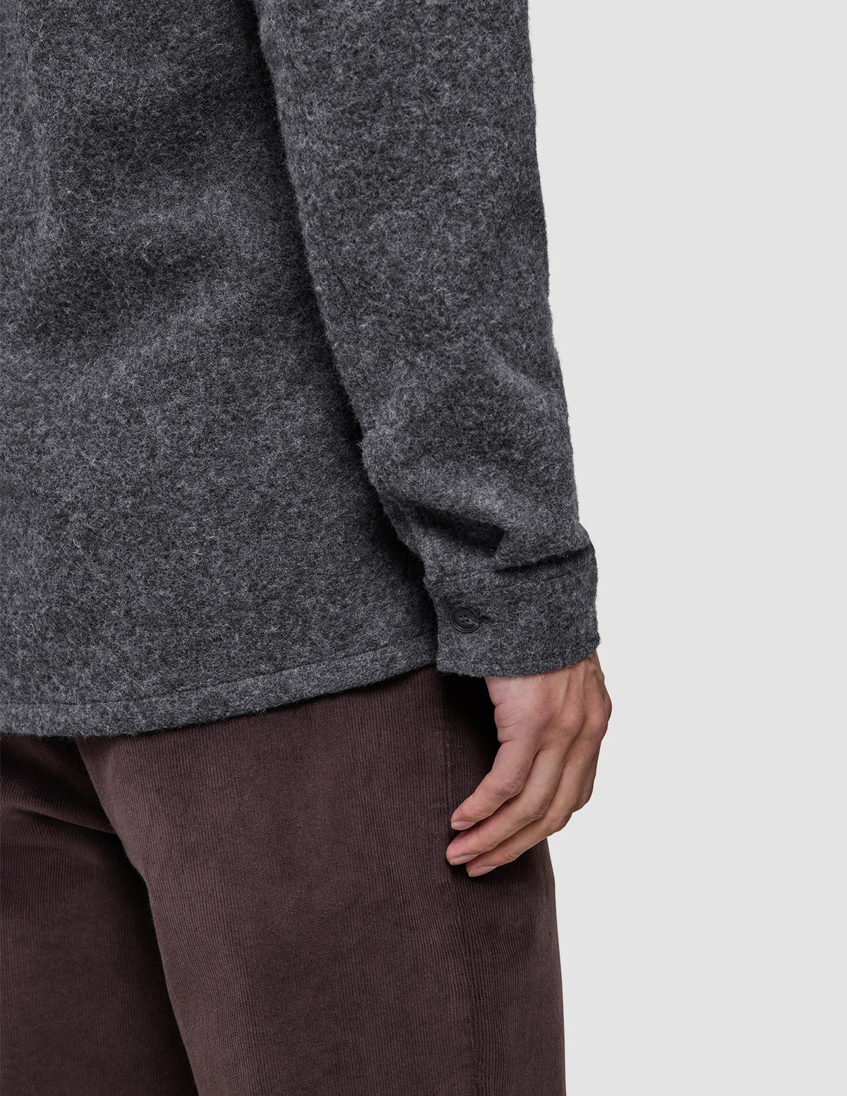 Nahaufnahme einer Person, die ein dunkelgraues, doppellagiges Woll-Overshirt in regulärer Passform mit geknöpften Manschetten trägt, kombiniert mit einer braunen Hose.