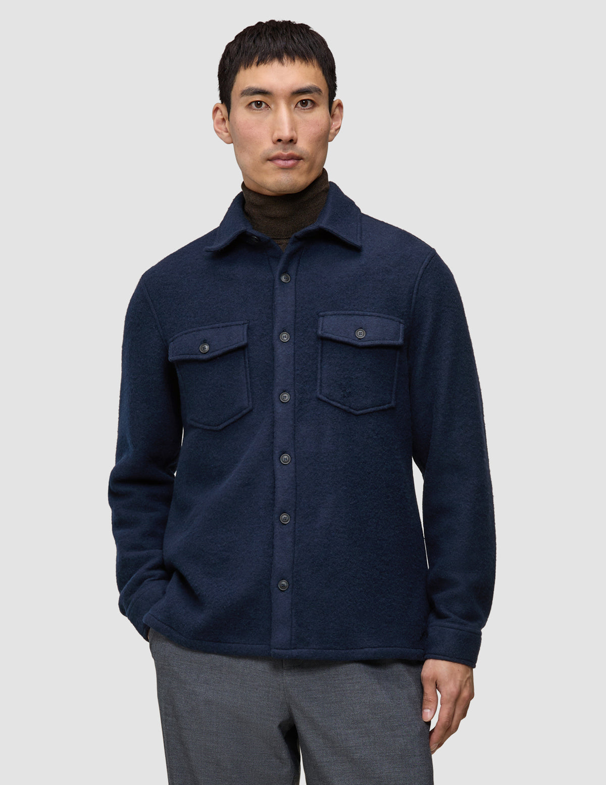 Eine Person, die ein doppellagiges Woll-Overshirt in der Farbe Regular Dark Navy über einem dunkelbraunen Rollkragenpullover trägt und damit klassisches skandinavisches Design zur Geltung bringt.